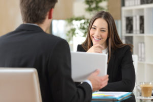 Salesman showing product from a tablet to a happy client who is looking at device in an office indoor